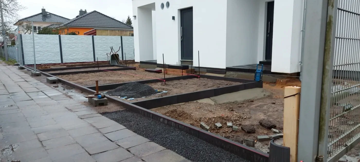 Rohzustand am Doppelhaus mit gesetzten Randsteinen und Betonzaun zur Straße