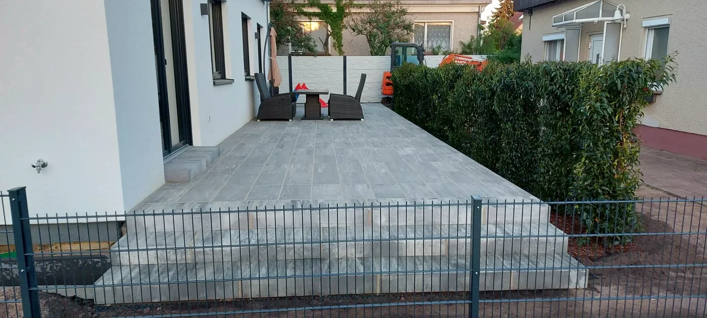 Fertige Terrasse mit Gartenmöbeln, Stufe zum Garten und Kirschlorbeerhecke