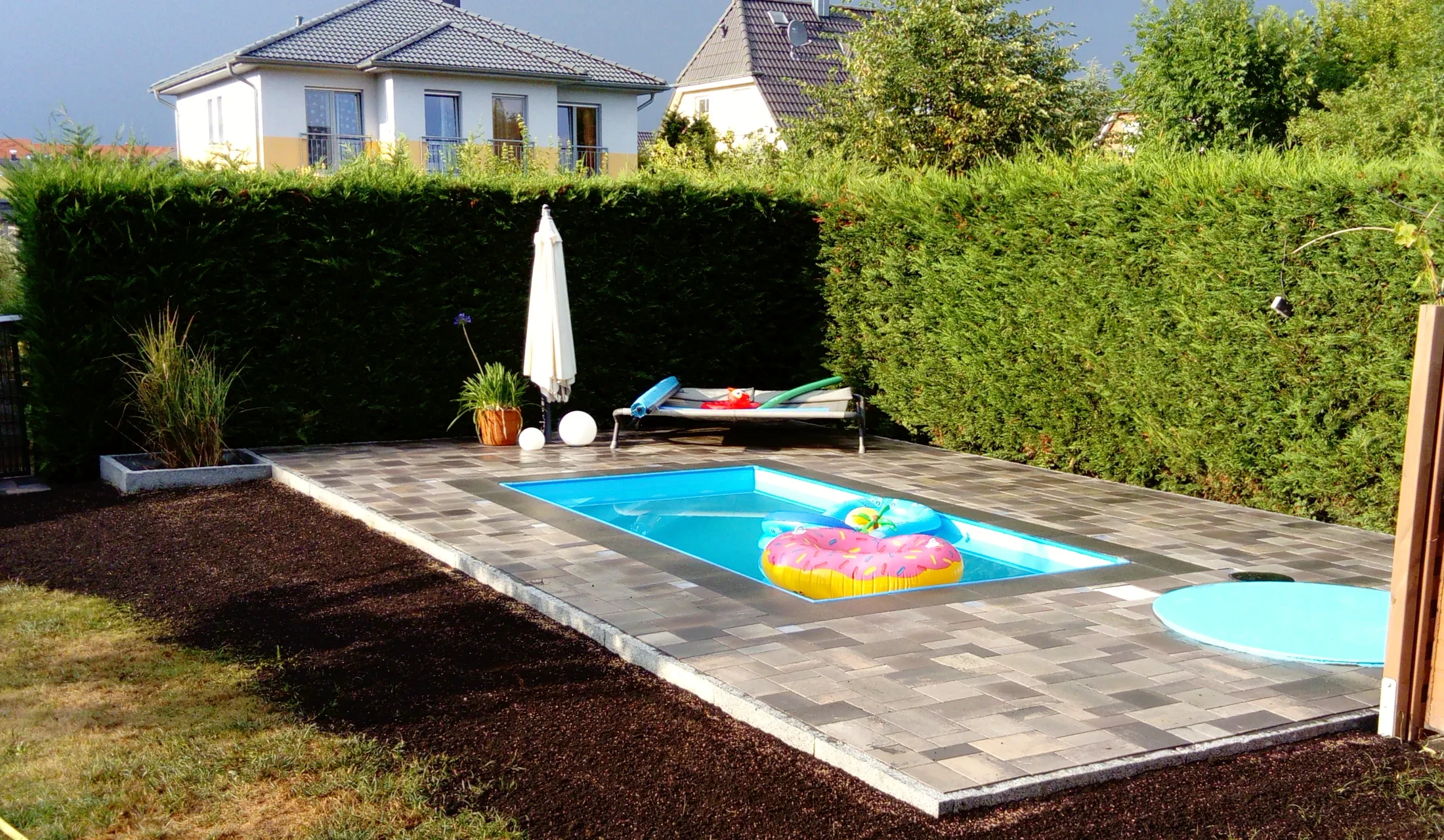 Pool mit gepflasterter Umrandung, Liegefläche und hoher Hecke
