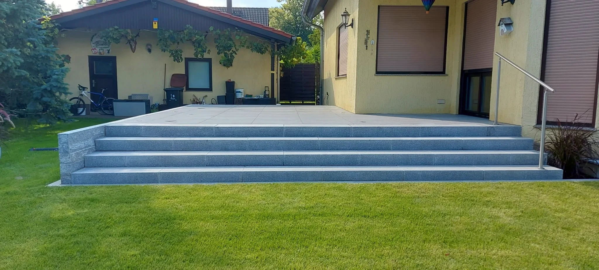 Erhöhte Terrasse mit Granitstufen und frisch verlegtem Rollrasen nach einer Poolsanierung
