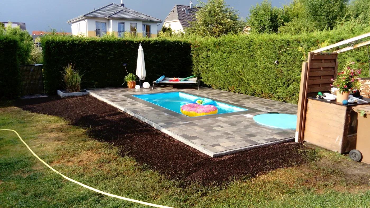 Neu angelegte Außenanlage mit Pool, gepflasterter Umrandung und Sichtschutz an einer Thujahecke