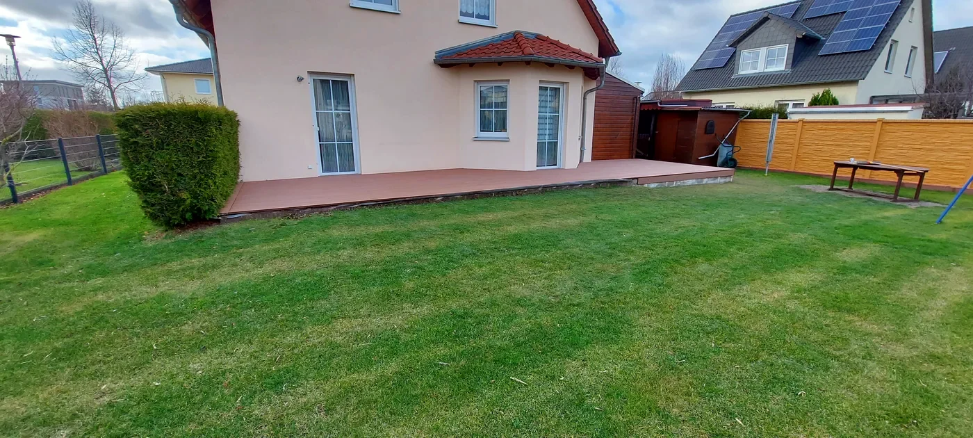 Fertige Rasenfläche mit angrenzender WPC-Terrasse an einem Einfamilienhaus