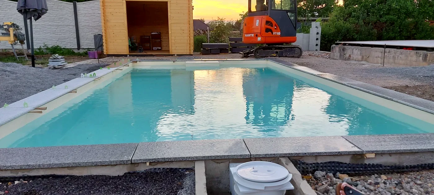 Neu gebauter Pool mit Granit-Umrandung im Abendlicht, daneben ein Minibagger