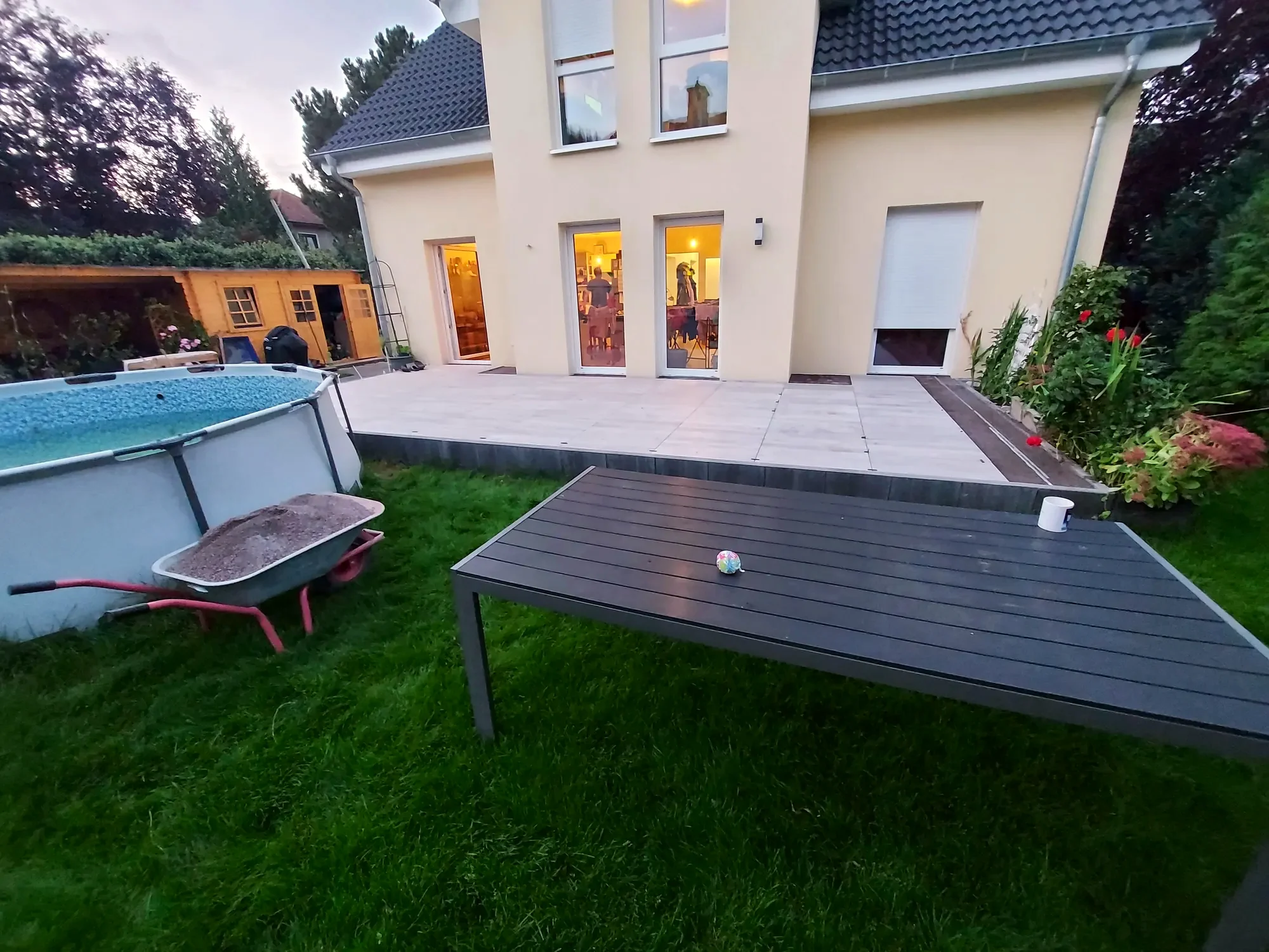 Fertige Terrasse mit Gartenmöbeln vor einem beleuchteten Wohnhaus in der Abenddämmerung