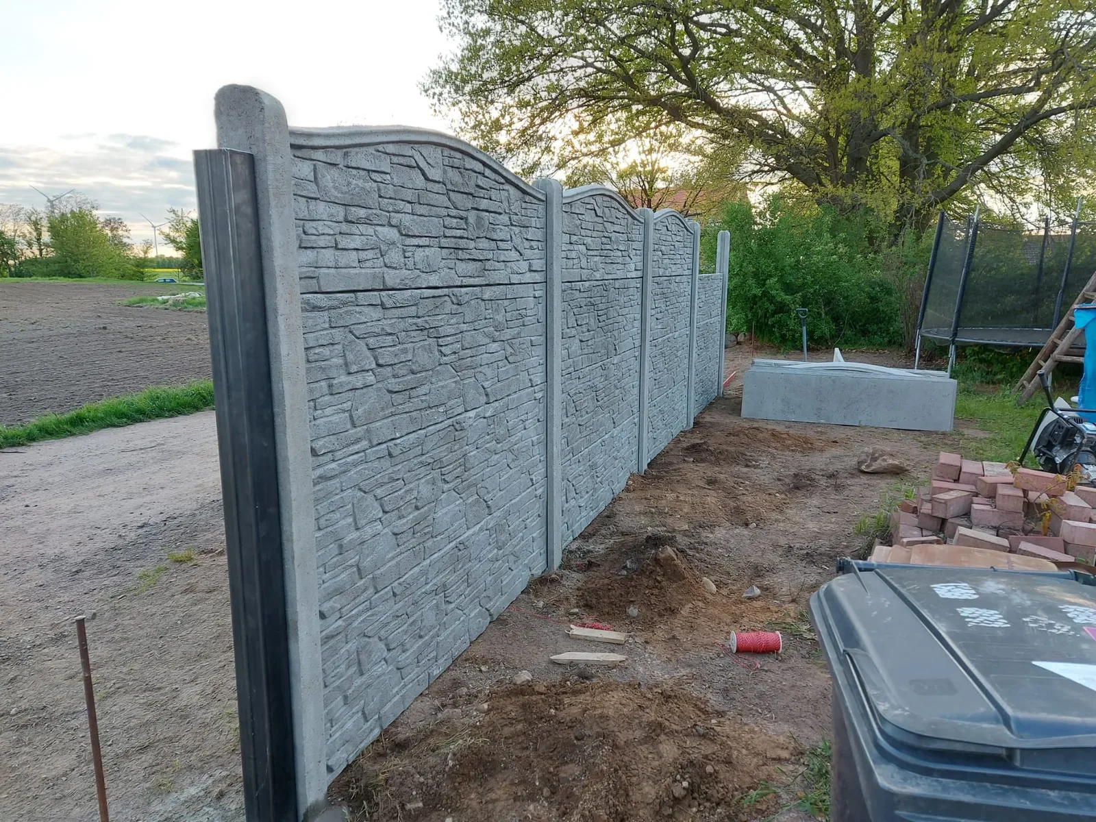 Grauer Betonzaun mit geschwungenem Abschlusselement an einer Grundstücksecke