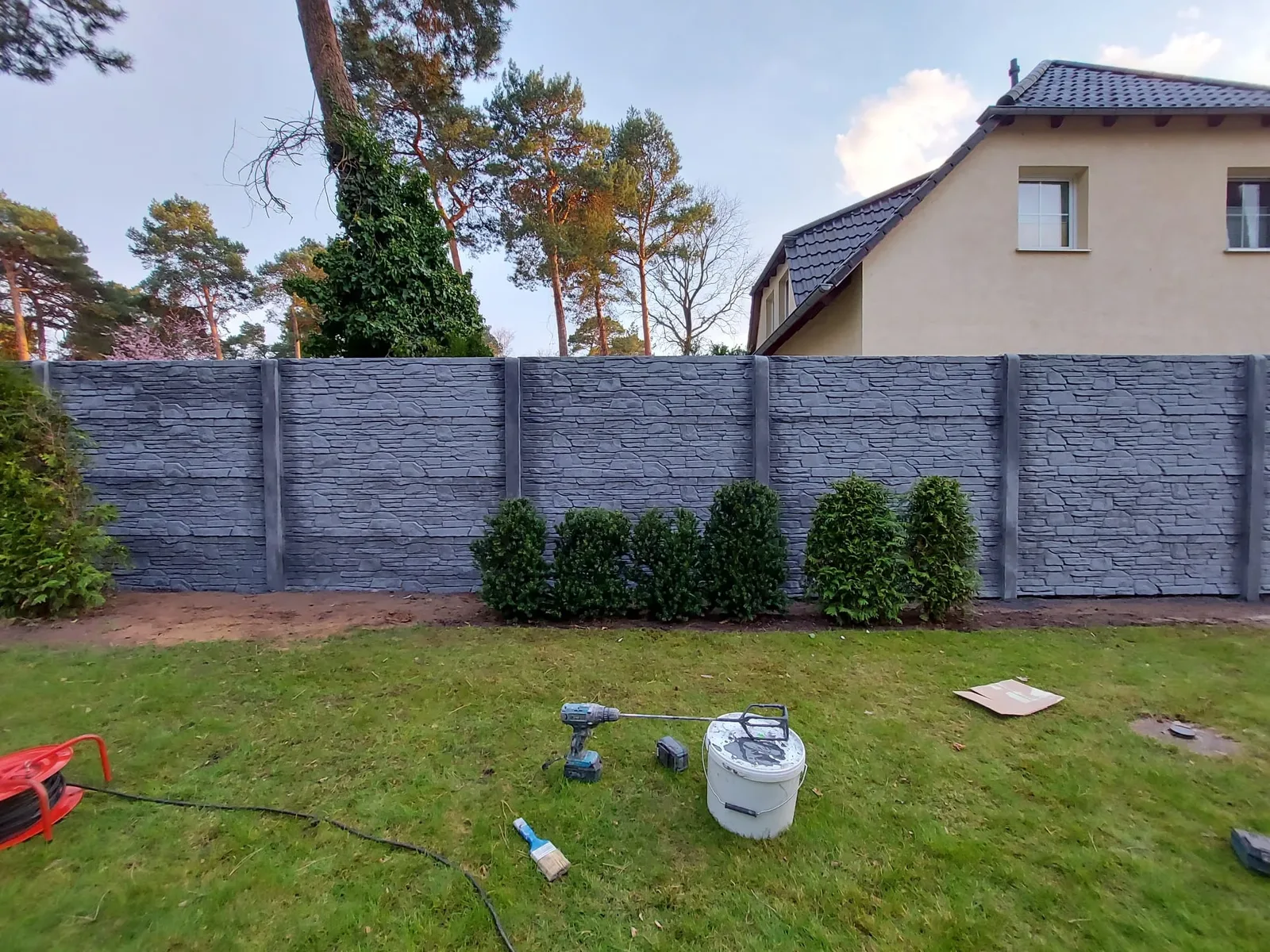 Anthrazitfarbener Betonzaun in Bruchsteinoptik mit neu gepflanzter Hecke davor