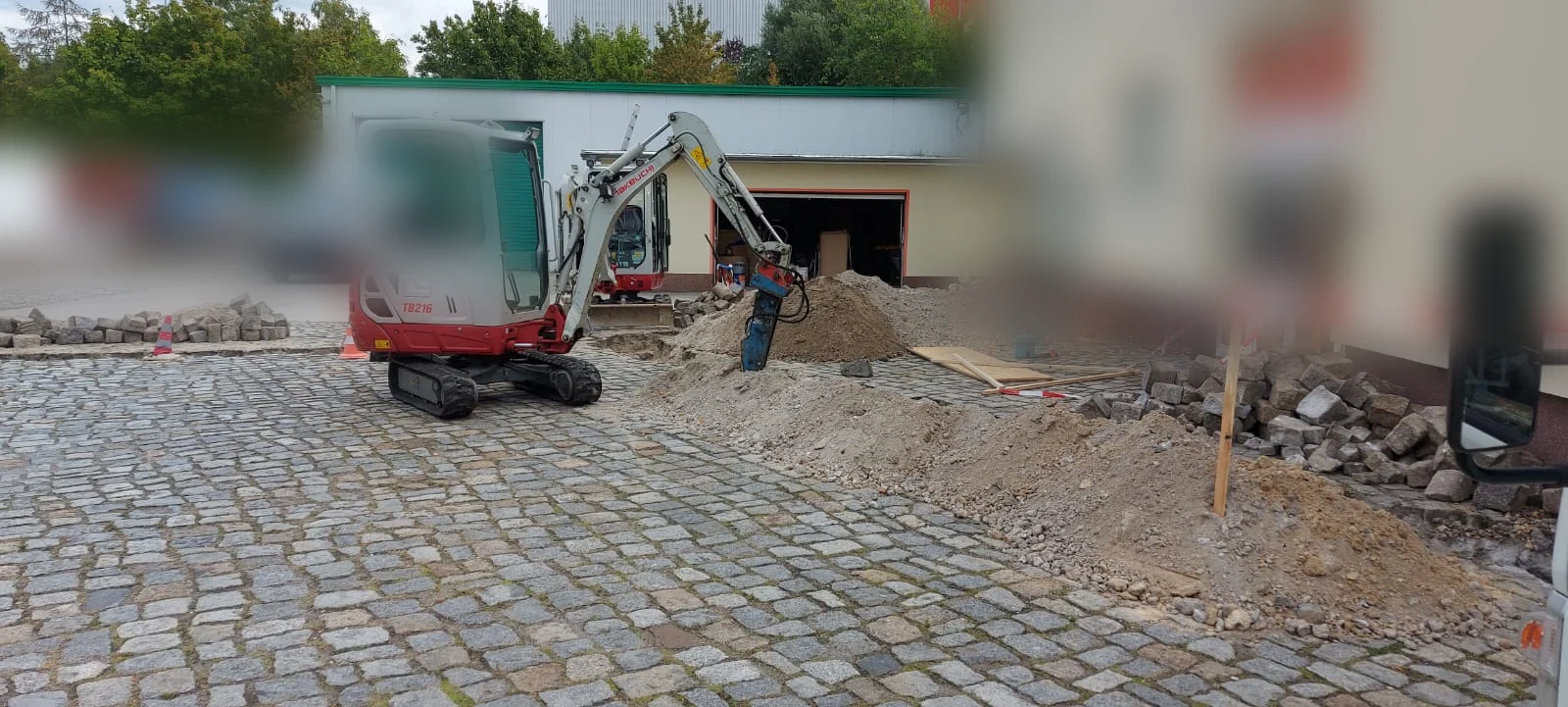 Minibagger mit Hammeraufsatz beim Aufbrechen einer Pflasterfläche für einen Leitungsgraben