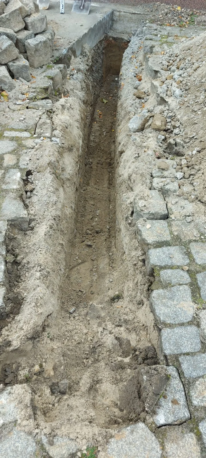 Ausgehobener Leitungsgraben zwischen Bordsteinen mit freigelegtem Schotterunterbau