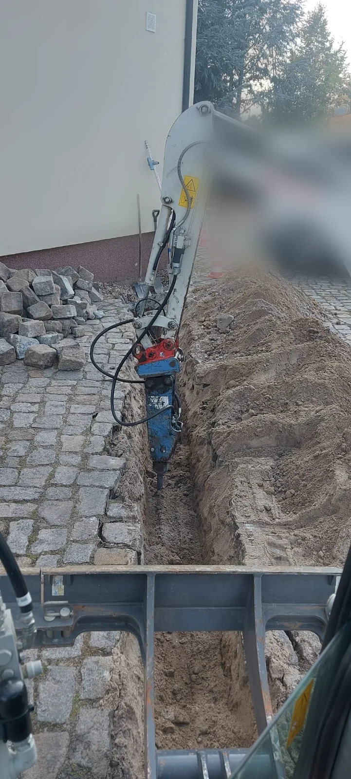 Hammerbagger arbeitet einen schmalen Leitungsgraben im Kopfsteinpflaster frei