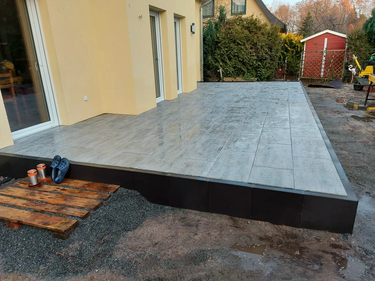 Hochterrasse mit großformatigen Platten und dunkler L-Winkeleinfassung an einem Wohnhaus