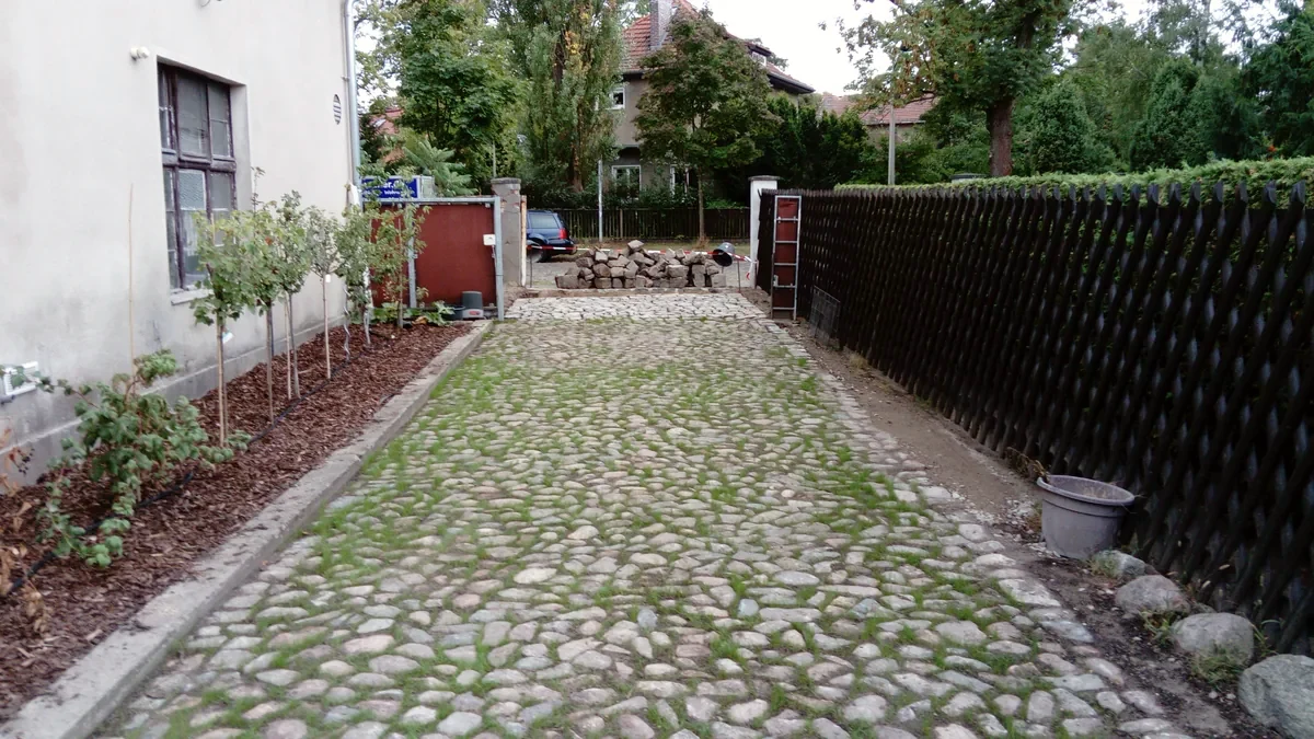 Einfahrt aus historischem Katzenkopfpflaster mit begrünten Fugen