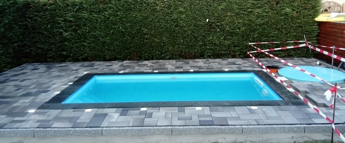 Swimmingpool mit anthrazitfarbener Pflasterumrandung und eingelassenen Bodenleuchten