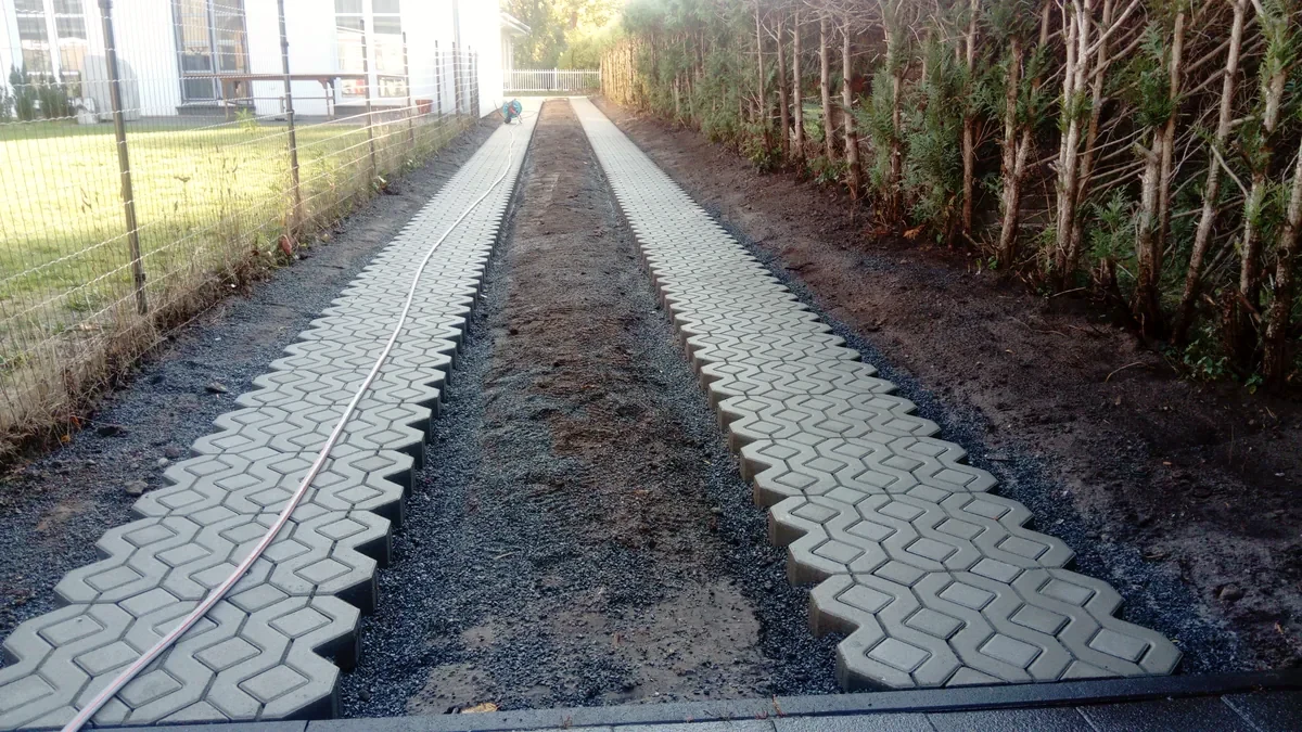 Zwei Fahrspuren aus Rasengittersteinen mit Füllsteinen zwischen Hecken