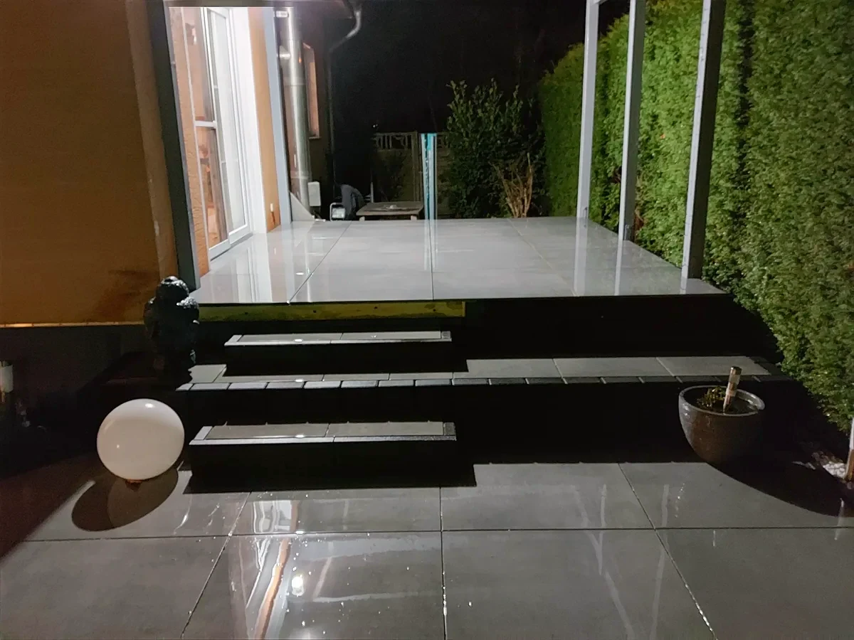 Beleuchtete Terrassentreppe mit hellen Platten und dunklen Blockstufen bei Nacht